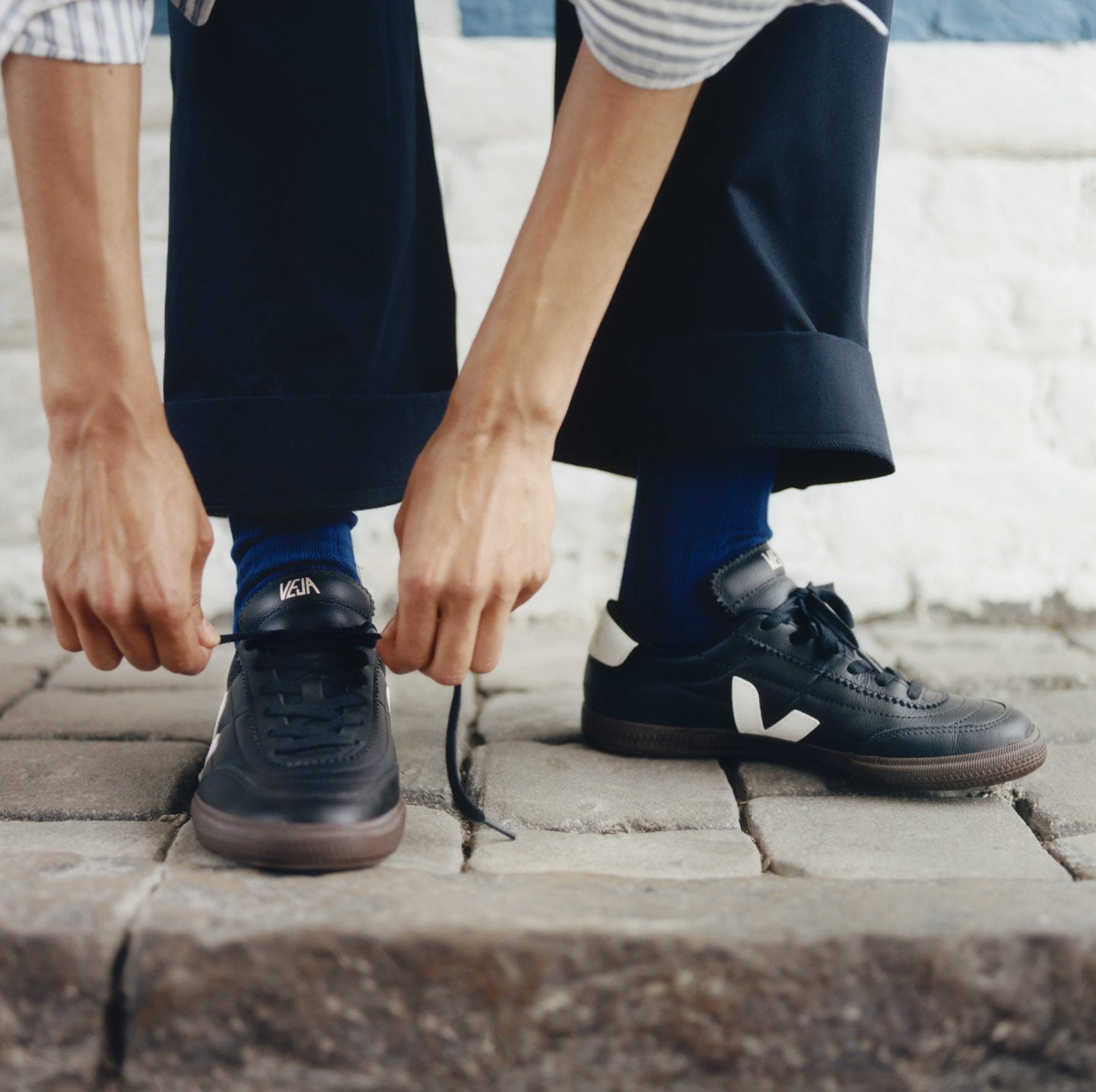 Man fastening laces of Veja Panenka black trainers